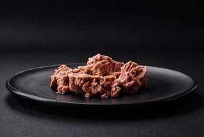 Delicious canned tuna meat on a black ceramic plate on a dark concrete background photo