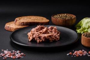 Delicious canned tuna meat on a black ceramic plate on a dark concrete background photo