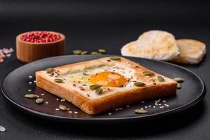 huevo frito en forma de corazón en pan tostado con semillas de sésamo, semillas de lino y semillas de calabaza en un plato negro foto