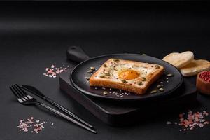 Heart shaped fried egg in bread toast with sesame seeds, flax seeds and pumpkin seeds on a black plate photo