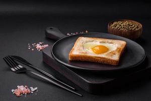 Heart shaped fried egg in bread toast with sesame seeds, flax seeds and pumpkin seeds on a black plate photo