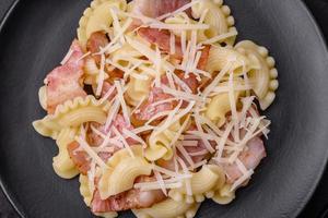 Delicious pasta with bacon and parmesan cheese on a black ceramic plate photo