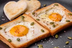 huevo frito en forma de corazón en pan tostado con semillas de sésamo, semillas de lino y semillas de calabaza en un plato negro foto