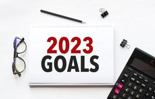 Business concept. Notebook with text goals 2023 sheet of white paper for notes, calculator, glasses, pencil, pen, in the white background photo
