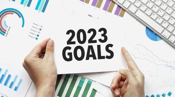 hand holding paper with text goals 2023 with charts and keyboard photo