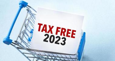 Shopping cart and text tax free 2023 on white paper note list. Shopping list concept on blue background. photo