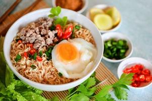 noodles bowl with boiled egg minced pork vegetable spring onion lemon lime lettuce celery and chili on table food , instant noodles cooking tasty eating with bowl - noodle soup photo