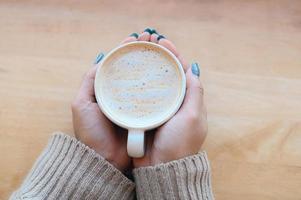 top view coffee caramel woman coffee with hand holding a cup on the wood table, caramel coffee cup in the morning - hot caramel macchiato photo
