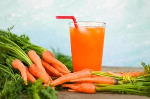 jugo de zanahoria en el fondo de la mesa de madera, zanahorias frescas y dulces para cocinar frutas y verduras para el concepto de salud, jugo de zanahorias frescas en vidrio con hielo en verano foto