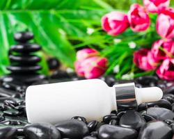 Cosmetic white bottle for essential oils on black stone photo