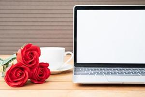 rosa roja y taza de café con maqueta de portátil en madera foto