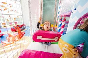 Happy sisters playing at indoor play center playground. Girl in swing. photo