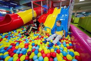 Happy kids playing at indoor play center playground. Children slides in colored slide into balls in ball pool. photo