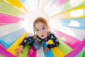 Funny girl playing at indoor play center playground in colored tube. photo