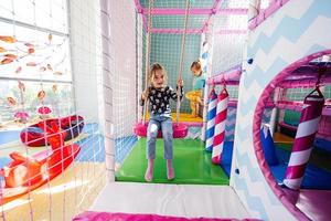 Happy sisters playing at indoor play center playground. Girl in swing. photo