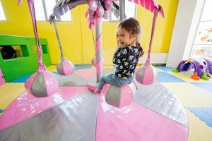 Happy girl playing at indoor play center playground,  swing on palm. photo