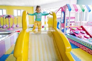 Happy girl playing at indoor play center playground. Sliding in yellow slide. photo