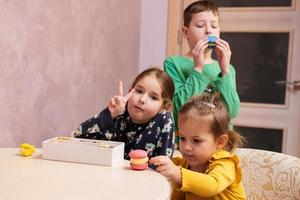 tres niños comen deliciosos y sabrosos macarons de color dulce. foto