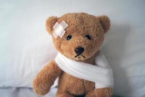 Sad bear doll lying sick in bed with the wound on the head and bandage photo