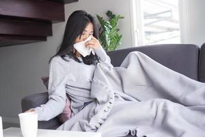mujer enferma con dolor de cabeza sentada bajo una manta con tos, estornudos, infecciones estacionales, gripe, alergias tendida en el sofá con una manta de fiebre alta y gripe foto