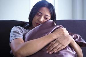 la mujer se sentó y abrazó la almohada en el sofá de la casa. la expresión y el desánimo y la desesperación. foto