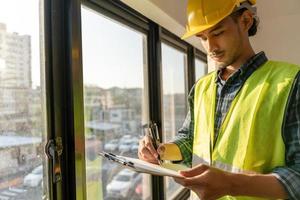 el inspector o ingeniero está inspeccionando la construcción y el aseguramiento de la calidad de la nueva casa usando una lista de verificación. ingenieros o arquitectos o contratistas trabajan para construir la casa antes de entregársela al propietario foto