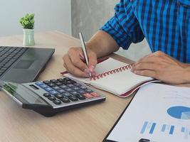 Man hand is writing a calculations record with a statistical graph. photo