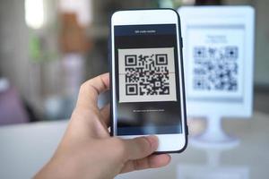 Women's hand uses a mobile phone application to scan QR codes in stores that accept digital payments without money and plastic tags on the table. QR code payment and cash technology concept photo