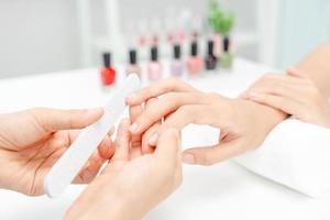 la mujer recibe el servicio de atención de la manicura esteticista profesional en el centro de spa. el salón de belleza de uñas usa una lima de uñas para el tratamiento de acristalamiento. manicurista hace que el cliente de uñas sea hermoso. tratamiento de spa para el cuidado del cuerpo foto