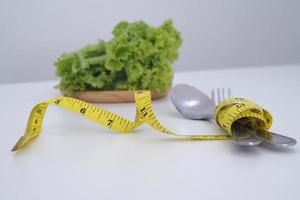 lechuga y cinta métrica envuelta alrededor de una cuchara y un tenedor. concepto de alimentación y dieta saludable foto