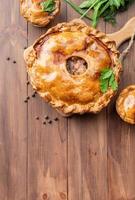 Homemade meat pie with greenery on wooden background photo