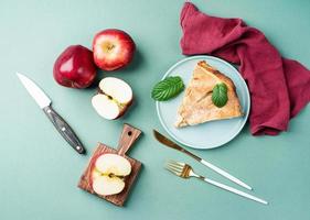 Homemade piece of apple pie with fresh red apples on green table photo