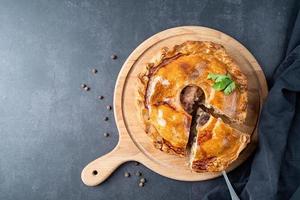 Homemade meat pie with greenery on wooden cutting board on dark table photo