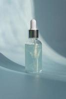 Cosmetic spa medical skincare, glass serum bottle with marine collagen on blue background with sun shadows. Unbranded Cosmetic product presentation. copy space photo