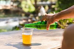 hombre vertiendo cerveza en vaso de plástico de una botella durante las vacaciones. foto