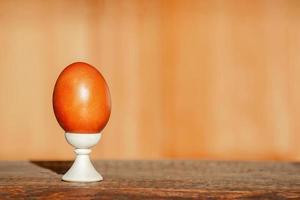 on a wooden background, one painted Easter red egg stands on a stand with natural dyes in the rays of the bright sun, minimalism, copy space. Preparing to celebrate Easter photo