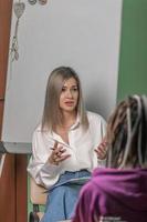 A beautiful female psychologist works in her office with a young girl client with dreadlocks on her head. In the hands of a specialist are the notes that she makes during the consultation photo