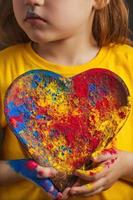 las manos de los niños sostienen un plato de madera en forma de corazón en el que los colores brillantes multicolores de holi. festival indio de colores holi. foto