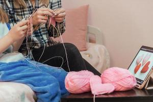 mother teaches her daughter to knit, in front of them is a tablet with a training video, they knit bright pink hearts. congratulations on mother's day, happy valentine's d photo