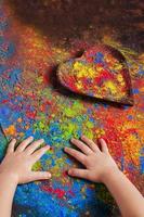 children's hands lie on a table on which Holly's paints are scattered and a wooden plate in the shape of a heart, in which bright colors, copy space. Indian festival of colors Holi photo