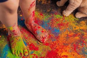 children's feet strewn with multi-colored bright Holi colors and cat paws nearby, copy space. Indian festival of colors Holi. photo