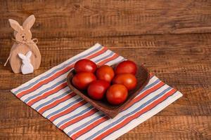 sobre un fondo de madera huevos de pascua pintados con pinturas vegetales naturales con cáscara de cebolla, junto a un conejo de pascua de madera y sauce, preparación para las vacaciones de pascua foto