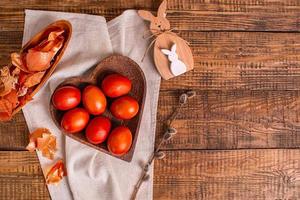 sobre un fondo de madera huevos de pascua pintados con pinturas vegetales naturales, cáscara de cebolla, junto a un conejito de pascua de madera y sauce, vista superior, espacio para copiar foto