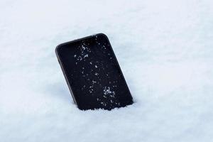 teléfono móvil perdido en el concepto de nieve. de cerca. pantalla de dispositivo en blanco con copos de nieve foto