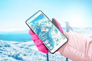 Ski map on phone display in hand with glove. Ski poles and mountain in background photo