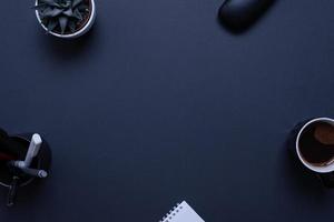 Professional black desk with plant, pens, coffee mug, glasses box, and pad,. Top view, flat lay composition for copy or product presentation photo