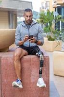 Sportsman with prosthetic leg sitting on block and using cellphone photo