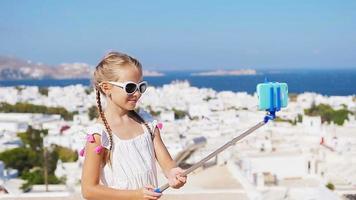 Adorable little girl taking selfie photo background Mykonos town in Greece video