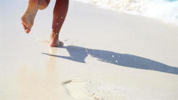 Nahaufnahmebeine, die im seichten Wasser am weißen Strand entlang laufen. konzept von strandurlaub und barfuß. Zeitlupe. video