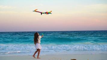 Adorable little girl with flying kite on tropical beach. Happy kid playing on ocean shore with beach kite. Slow moion video